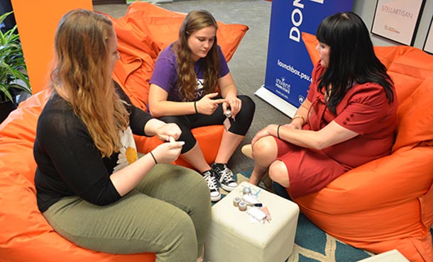 Paige Speckhart, Kylie Kinlough, and Janna Maranas (left to right) gather at the LaunchBox to discuss progress of their cosmetics line.