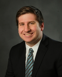 head and shoulder shot of Drew Carson in a suit and tie on dark background